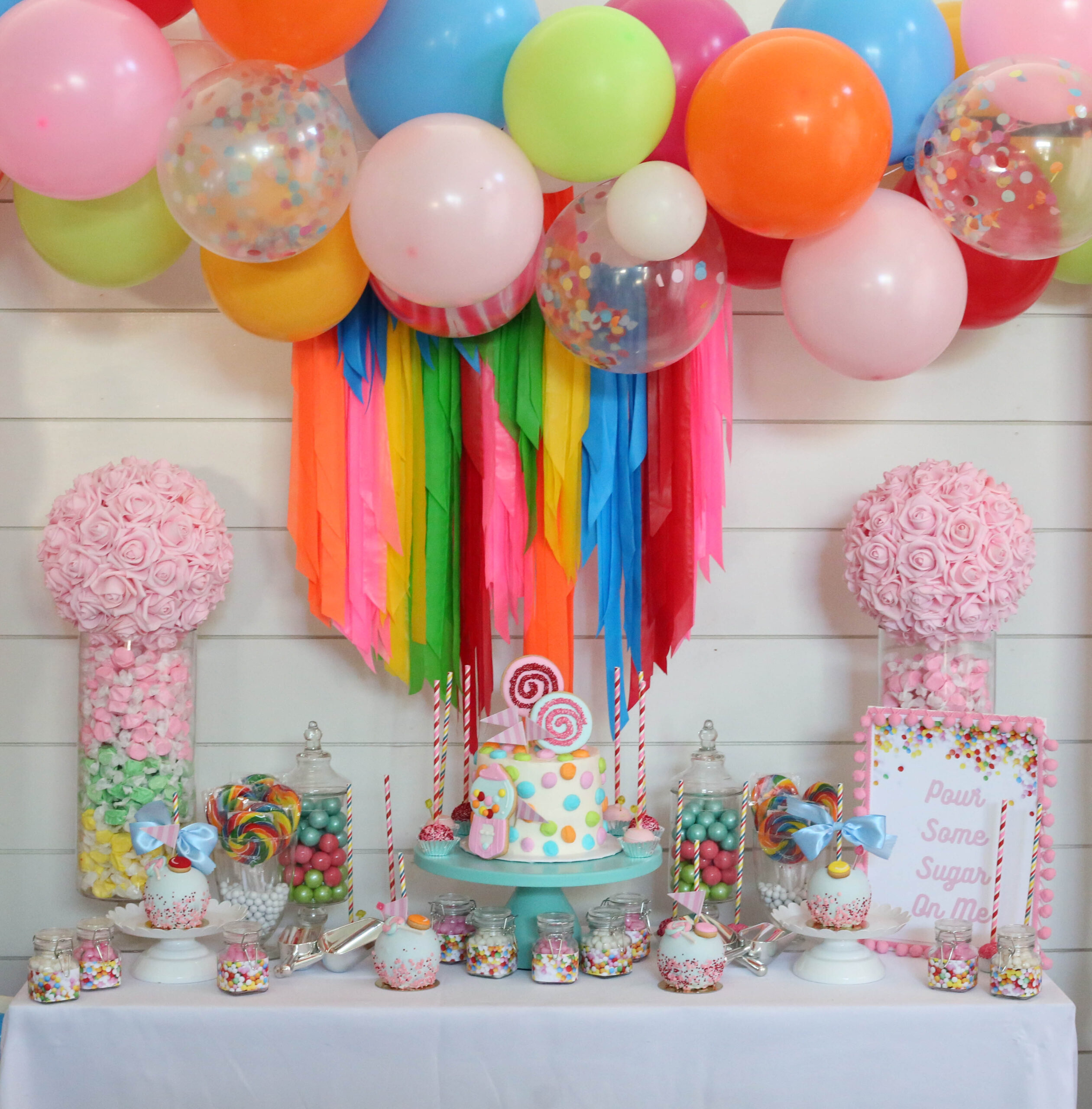 candy themed party backdrop display with balloon garland and rose balls
